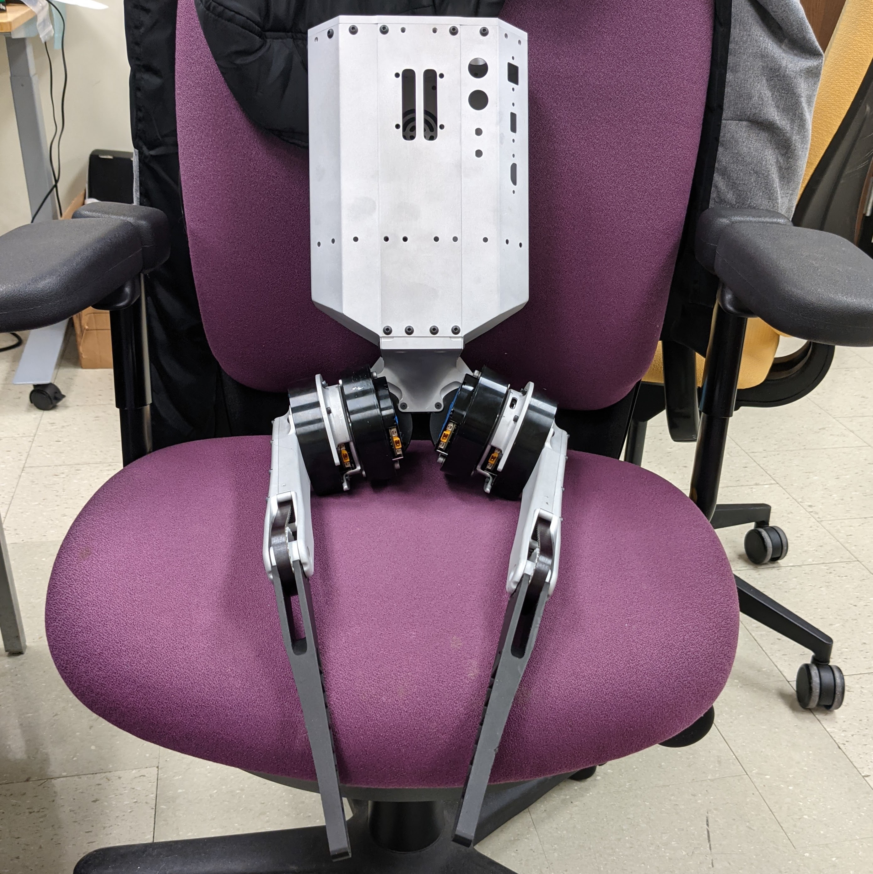 Photo of a small bipedal robot sitting on an office chair with its legs crossed.
